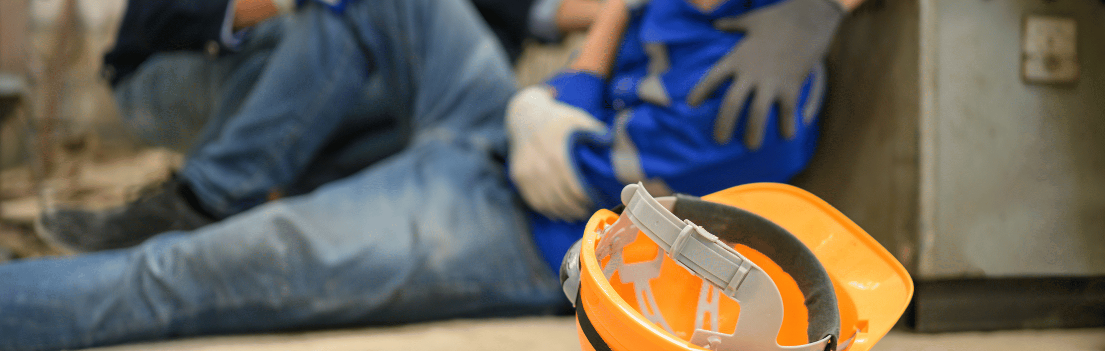 Construction worker sitting on the floor in blue coveralls with white gloves, orange hard hat in the foreground.